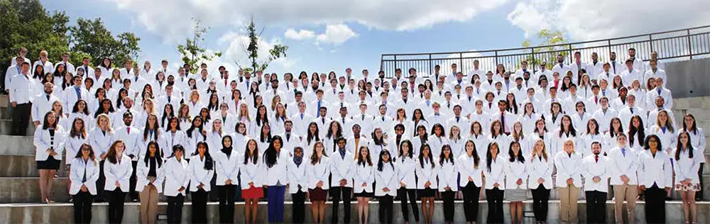 Large group of medical students standing in stadium style rows wearing newly received white coats.