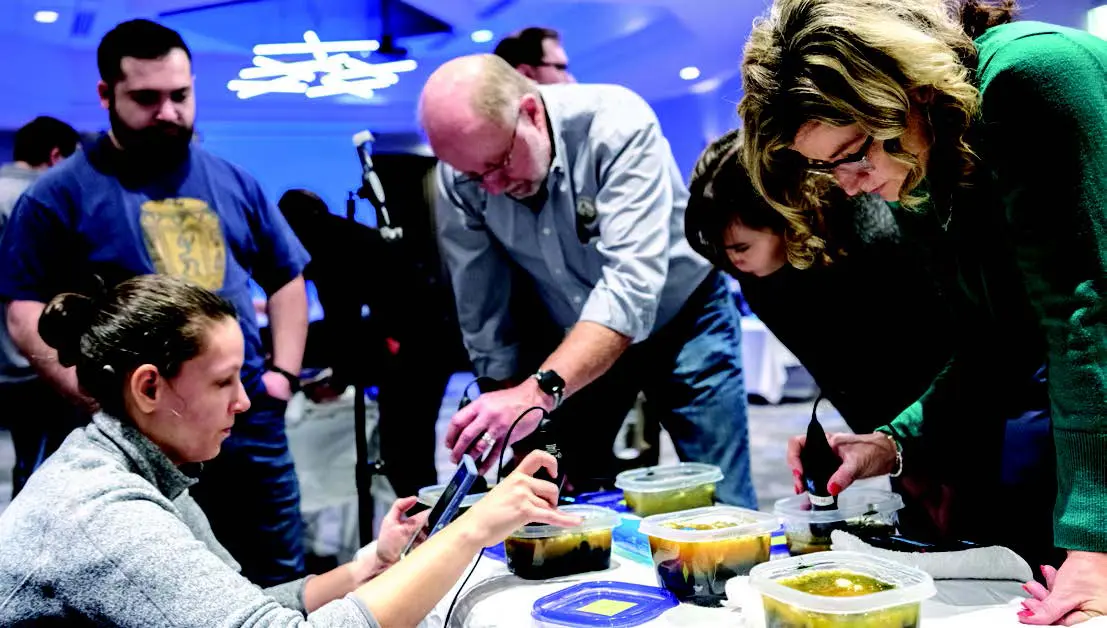 people leaning over a table with containers of unknown substance and testing equipment