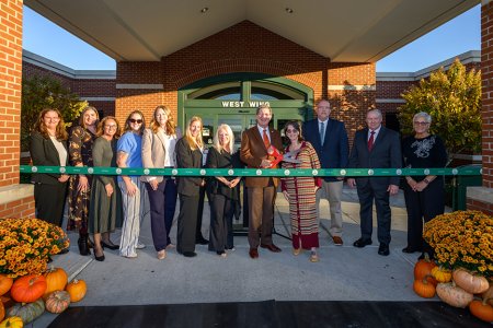 Twelve people stand behind a ribbon that is about to be cut
