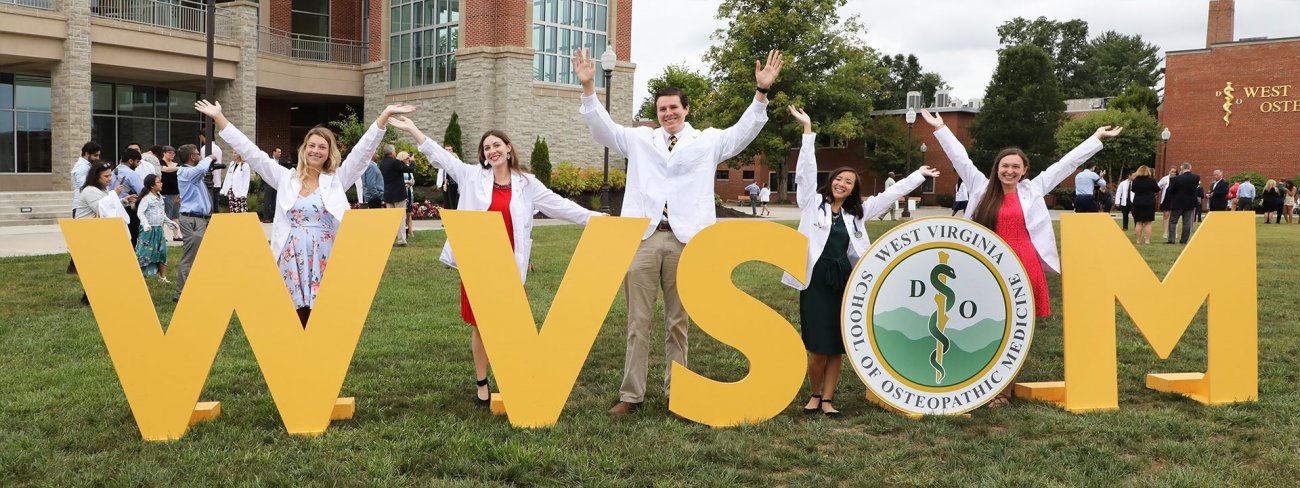 Students in White Coats behind large WVSOM letters