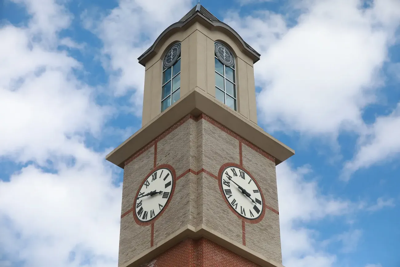 WVSOM Clock Tower top with blue sky and scattered white clouds in background