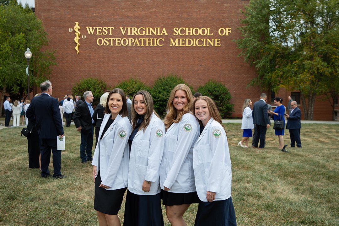 Students in white coats stand on parade field